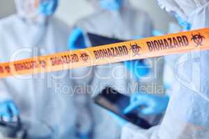 Closeup on biohazard quarantine tape. Hands of scientist using a digital tablet behind covid barrier. Medical professional working in a biohazard crime scene. Doctors working behind caution tape