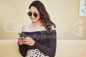 Fashionable young mixed race woman with sunglasses using her smartphone while standing on sidewalk. Millennial woman sending a text or chatting on social media while on city street