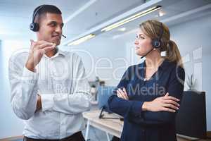 Mixed race call centre telemarketing agent discussing plans with caucasian colleague while working together in an office. Two consultants troubleshooting solution for customer service and sales support