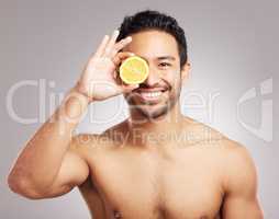 Handsome young mixed race man posing with an orange slice isolated in studio against a grey background. His skincare regime keeps him fresh. Eating healthy vitamins and nutrients for firm skin