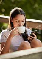 Coffee and social media go together. an attractive young woman sitting alone outside and enjoying a cup of coffee while using her cellphone.