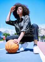 Low view of a young confident mixed race woman basketball player standing on the court getting ready to play. Hispanic female basketball player a day on the court looking stylish with her curly afro hair style against a urban background