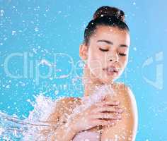 Deadly fresh. Shot of a beautiful young woman being splashed with water against a blue background.