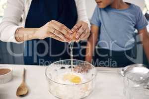 Closeup of female hands cracking a egg into a bowl while baking at home with her son. Woman adding ingredients to a glass bowl on the counter at home while baking with her child