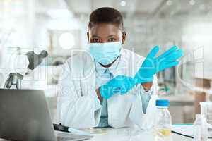 Im ready to work with samples. Shot of a young scientist sitting alone in her laboratory and putting surgical gloves on.