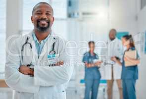 Mature african american male doctor standing with his arms crossed while working at a hospital. One expert medical professional smiling while standing at work at a clinic