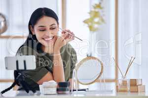 Young beauty blogger smiling while looking into a vanity mirror and doing a make-up tutorial while recording with her smart phone. Influencer sharing her beauty products and tips on social network