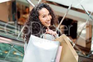 Portrait beautiful mixed race woman standing on an escalator while shopping in a mall. Young hispanic woman carrying bags, spending money, looking for sales and getting in some good retail therapy