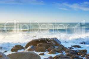 Waves crashing onto a rocky shore. A seascape view of the ocean with blue sky copy space in Camps Bay, Cape Town, South Africa. Calm, serene and tranquil beach with relaxing scenery in nature
