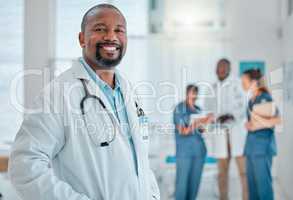 Happy mature african american male doctor standing while working at a hospital with colleagues. Expert medical professional smiling while at work at a clinic with coworkers