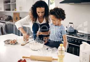 Mixed race woman standing and teaching her adorable little son how to bake in a kitchen at home. Cute hispanic boy helping his mother cook. African American parent bonding with her child on a weekend