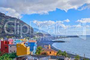 A colorful and vibrant city Port of Tazacorte, La Palme, Spain. Beautiful landscape of an urban town near the beach and mountains with a cloudy blue sky. Bright buildings near the sea or ocean