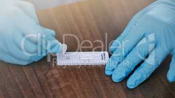 Unrecognizable doctor wearing gloves and preparing a covid test on a table while working at a hospital. Closeup of an unrecognizable gp working on a covid test at a desk in an office at a clinic