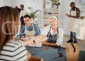 Joyful mature caucasian clothing designer talking and giving a customer a package in a shop at work. Customer making a purchase from a female clothing designer at a boutique