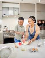 Hes going to put me out of Mommy duties soon. Shot of an attractive young mother bonding with her son and helping him bake in the kitchen at home.