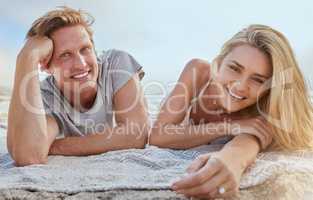 Portrait of happy young couple lying on blanket and enjoying beach vacation. Smiling young blonde man and woman relaxing on shore and enjoying their honeymoon or romantic date on a summers day