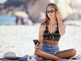 One beautiful young caucasian woman relaxing and listening to music while sitting on the beach. Enjoying a summer vacation or holiday outdoors in the day. Taking time off and getting away from it all