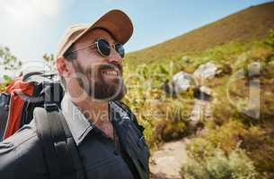 Fit adventurous man wearing glasses cap and a backpack while out hiking or exploring by the mountains. Handsome man with beard smiling while exploring nature on a sunny day