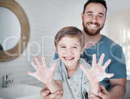 Germ free hands are happy hands. Portrait of a boy holding up his soapy hands while standing in a bathroom with his father at home.