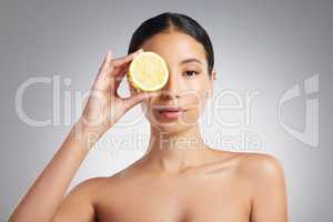 Studio Portrait of a beautiful young mixed race woman holding a lemon. Hispanic model using a lemon for oil control against a grey copyspace background