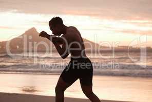 One african american man practicing shadow boxing on a beach at sunset. Black male focus on speed, strength and fitness while showing his muscular athletic shape against a sunrise copyspace background
