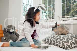 My fluffy friend. Shot of an adorable little girl using a digital tablet and bonding with her pet rabbit on her bed.