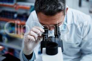 He misses nothing. a mature man using a microscope while conducting pharmaceutical research.