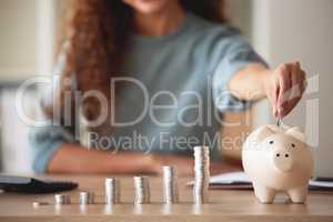 Young african american woman money putting coins into a piggybank at home. Mixed race person counting coins while financial planning in her living room. Saving, investing and thinking about the future