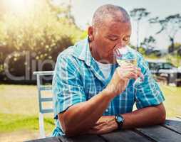 One senior mixed race man sitting alone and drinking glass of white wine during wine tasting on a vineyard. Elderly hispanic man holding and enjoying alcohol from a wineglass on farm during a weekend
