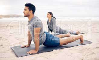 Opening up the chest while stretching the back. Shot of a sporty young couple doing an upward facing dog pose while practising yoga together on the beach.