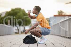 An African American man drinking water on a bridge. A man taking a break from exercising drinking from a bottle. A sporty guy focusing on health.