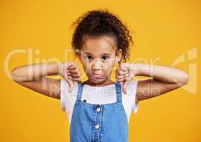 Studio portrait mixed race girl giving thumbs .down isolated against a yellow background. Cute hispanic child posing inside. Unhappy and upset kid being negative and saying, I disagree or disapprove