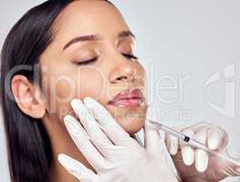 Beauty is pain. Shot of a woman having her lips injected with filler against a studio background.