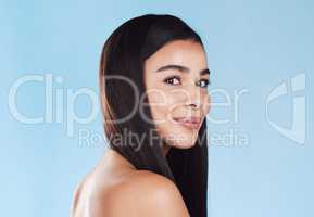 Portrait of one beautiful young hispanic woman with healthy skin and sleek hair smiling against a blue studio background. Happy mixed race model with flawless complexion and natural beauty