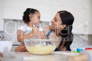 Happy mixed race mother and daughter baking and bonding. Young woman helping her daughter bake at home. Smiling mother holding an egg, cooking with her daughter. Happy little mixing a bowl of batter