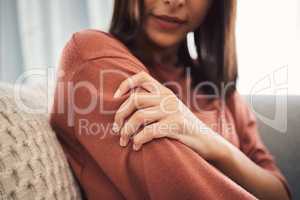 Close up of a young woman holding her arm and suffering with pain while sitting in the living room at home. Mixed race woman holding her arm in pain due to injury or arthritis