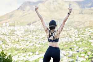 One mixed race woman from the back cheering with arms outstretched outdoors. Proud athlete celebrating victory and accomplishment after run or jog. Inspired and motivated to reach fitness and wellness goals