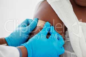 Hand of a doctor applying a plaster to a patients arm. Closeup of a doctor applying a plaster on a patient. African american patient being cared for by doctor. Medical professional in a consult