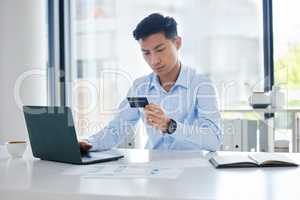 Closeup of one young asian businessman spending money online with a credit card and phone in an office. Making purchase transaction with secure banking payment. Budgeting finance for bills and e-commerce shopping