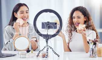 Two mixed race women recording a makeup tutorial for their beauty blog with a phone while sitting at home. Diverse young influencers live streaming their cosmetic review and recommendation online