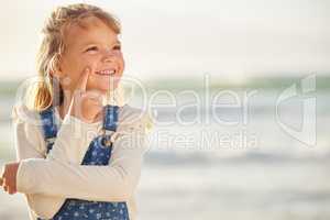 One adorable little girl thinking of ideas while standing on a beach outdoors. A cute young kid looking thoughtful while outside with the sea in the background. The mind and imagination on a child