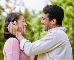 Loving husband putting hair behind wifes ear standing face to face in a park. Happy romantic moments of lovely couple spending time together outdoors. Man caressing womans face
