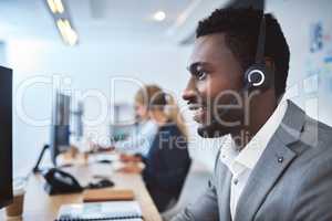 Happy young african american call centre telemarketing agent talking on a headset while working on computer in an office. Confident friendly male consultant operating helpdesk for customer service and sales support
