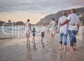 Rear view of Multi generation family holding hands and walking along the beach together. Caucasian family with two children, two parents and grandparents enjoying summer vacation