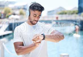 Fit young sportsman connecting his smart watch to his headphones to listen to music while out for a run or jog. Mixed race male athlete tracking his progress while exercising