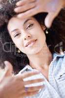 Beautiful young woman smiling and framing her face using her fingers from above. Happy hispanic woman with curly afro hair lying down creating frame around her face with hands and fingers