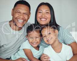 Portrait of a happy young mixed race family with two children wearing pyjamas and sitting at home together. Loving little sister and brother spending time with their parents on the weekend