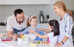 Happy young family with kids in kitchen preparing dough for pastry while spending weekend together at home. Loving caucasian family preparing home bakery