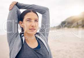 Ditch the boring gym routine for a refreshing beach workout instead. Shot of a sporty young woman stretching her arms while exercising on the beach.