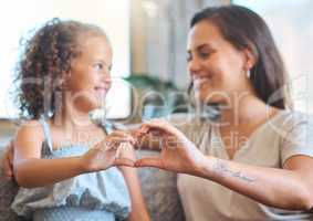 Loving mother and adorable daughter sitting together and forming a heart shape with their hands on the couch at home. Sweet moment between mother and child. Motherhood is fulfilling